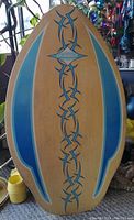 Front side of the wooden skim board showing blue tribal decal and Skimmer text.