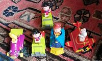 Five Peanuts character McDonald's toys from 1989 on carpeted floor, characters seated on colorful vehicles.