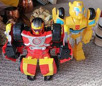 Two Transformers figures on carpet, yellow Bumblebee and red Lite Up Robot with large wheels on shoulders