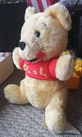 Front side of vintage Winnie the Pooh stuffed doll wearing red shirt with 'Pooh' embroidered.