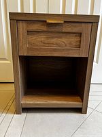 Front view of the nightstand showing one drawer with brass handle and open shelf below.