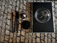 Disassembled pendant light parts including three black rods, ceiling mount base, light socket, and a clear glass globe shade on a carpeted floor.