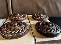 Four mahogany curtain holdbacks displayed on cardboard with detailed leaf carving and central raised button design.