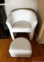 Front view of white barrel chair with ottoman separated in front of it on wood flooring