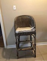 Front view of brown rattan bar stool with white cushion against wall.