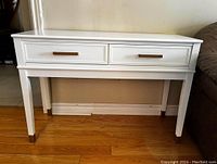 Front view of the white console table showing two drawers with gold-tone handles and gold accents on legs.