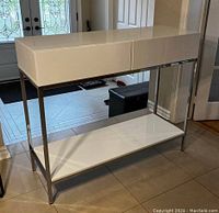 Side angle view of the white console table showing the metal frame and lower shelf.