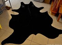 Black cowhide rug displayed flat on tiled floor, showing entire shape and edges.