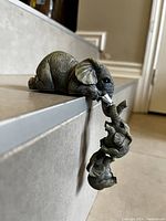 Mother elephant figurine lying on a tiled surface with four baby elephant figurines hanging vertically from her trunk.