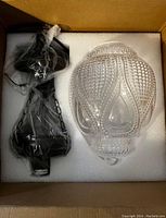 Photo of pendant light components in protective foam: clear glass shade and black iron hanging parts, wrapped and separated.