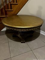 Front and side view of the gold round table showing the tabletop and carved base.
