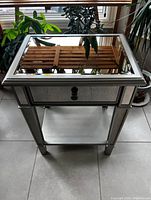 Front view showing the rectangular mirrored top and single drawer with knob, reflectivity of mirror surfaces visible.