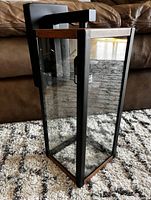 View of outdoor wall light fixture showing its rectangular shape, clear glass panels, and faux wood top and bottom accents.