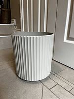 Front and side views of a white cylindrical ribbed planter with matte stone-like texture.