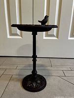 Full front view of a small cast iron bird bath showing the pedestal and bird figure on the basin edge.