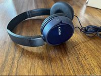 Close-up front view of blue Sony over-ear headphones, showing ear cups and headband, placed on wooden surface.