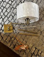 Steel wall sconce laid flat showing square mounting plate, swing arm, white fabric shade wrapped in plastic, and orange power cord.