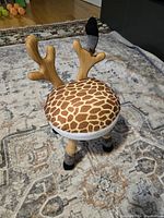 Toddler classroom chair with giraffe print padded seat, wooden antler backrest, and wooden legs with black tips, shot on patterned rug.