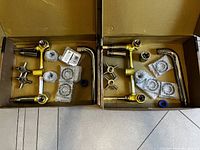 Two Kingston Brass faucet sets with components including cross handles, spouts, mounting rings, and seals packed in cardboard boxes.