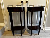 Front view of the two tall dark brown wooden side tables with rectangular tops and bottom shelves.
