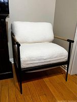 Left side view of the white upholstered armchair with black metal frame and wooden armrests on hardwood floor.