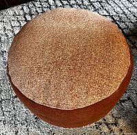 Top view of a round upholstered pouf showing woven beige and light brown fabric top