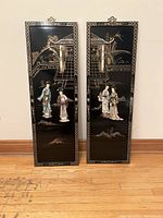 Pair of vertical rectangular black lacquer plaques side by side showing traditional Asian figures with mother of pearl and soapstone inlays and decorative borders.
