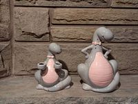 Front view of the ceramic dinosaur piggy bank and candle holder showing their gray and pink paint details and designs.