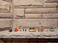 Overview of all 10 assorted small animal figurines in a row on a stone ledge against a stone wall background.