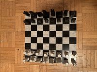 Overhead view of the complete chess set arranged on parquet flooring, showing black and white marble chess pieces on the marble board with standard checkered pattern.