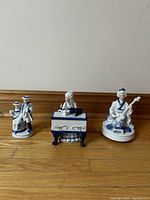 Three blue and white porcelain figurines: a Japanese woman playing a string instrument, a man sitting at a keyboard instrument, and a couple standing together.
