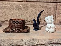 Brown textured ceramic container on matching tray, blue bird figurine, white pig figurine arranged side by side on stone surface against stone wall