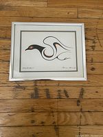 Framed print of a stylized loon titled Mother Bird Spirit by Clemence Wescoupe, shown flat on wood floor.