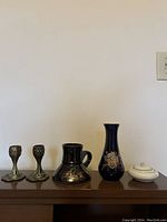 Full view of brass candleholders, black ceramic vessel, cobalt blue ceramic vase, and small white ceramic vessel with lid on wooden surface.