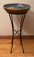Full view of ceramic bird bath on metal stand, showing bowl with floral design and four curved legs with center ring.