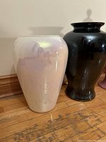 Two tall ceramic vases side by side on wooden floor, one iridescent white and one glossy black