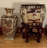 Photo showing both the decorative vase with floral design and the large planter bowl on a wooden stand side by side.