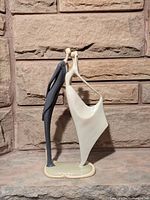 Front view of the elongated sculpture showing the couple kissing and the male figure in a blue suit with a female figure in a white flowing dress.