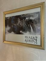 Framed Chinese landscape painting showing waterfalls and mountains with calligraphy in the top right corner, gold-tone frame visible.