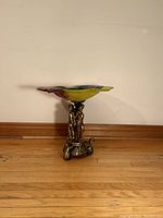 Side view of the vintage side table showing the flower-shaped glass top with multicolored vibrant glass and the brass base with three sculpted figures.