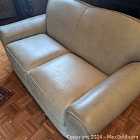 Front-side view showing tan leather-like suede upholstery of compact two-seat couch with piped edges and curved armrests.