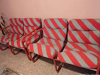 Three mid-century modern chairs lined up against wall, showing grey and red diagonal striped cushions with red tubular metal frames