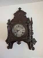 Front view of vintage ornate wooden clock showing clock face with Roman numerals and wood carvings.