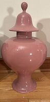 Front view of pink ceramic urn with lid showing bulbous shape and glossy finish.
