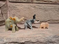 Three carved natural stone elephant figurines arranged by size from largest to smallest on a stone surface with a brick background