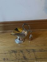 Side view of silver plated sugar scuttle with matching scoop on wooden floor.