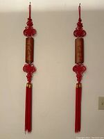 Pair of red lucky knot tassels hanging against a white wall, showing full length and design symmetry.