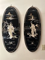 Full view of two oval black lacquered wall panels with mother-of-pearl inlay depicting female figures and scenic backgrounds