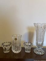 Photo showing the tall lead crystal vase and two matching smaller candle holders on a wooden surface against a plain wall