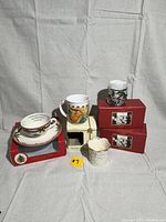 Lot contents with mugs, candle holders, and boxes on light fabric background.